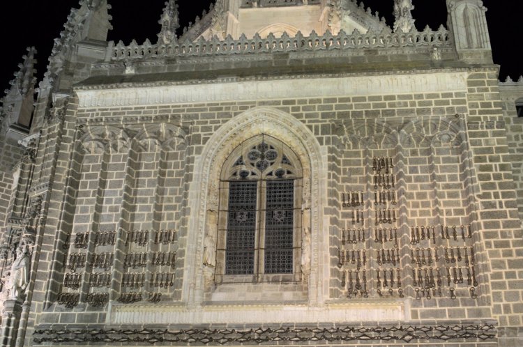 Vista nocturna de la fachada de San Juan de los Reyes, sobre la cual cuelgan decenas de cadenas.