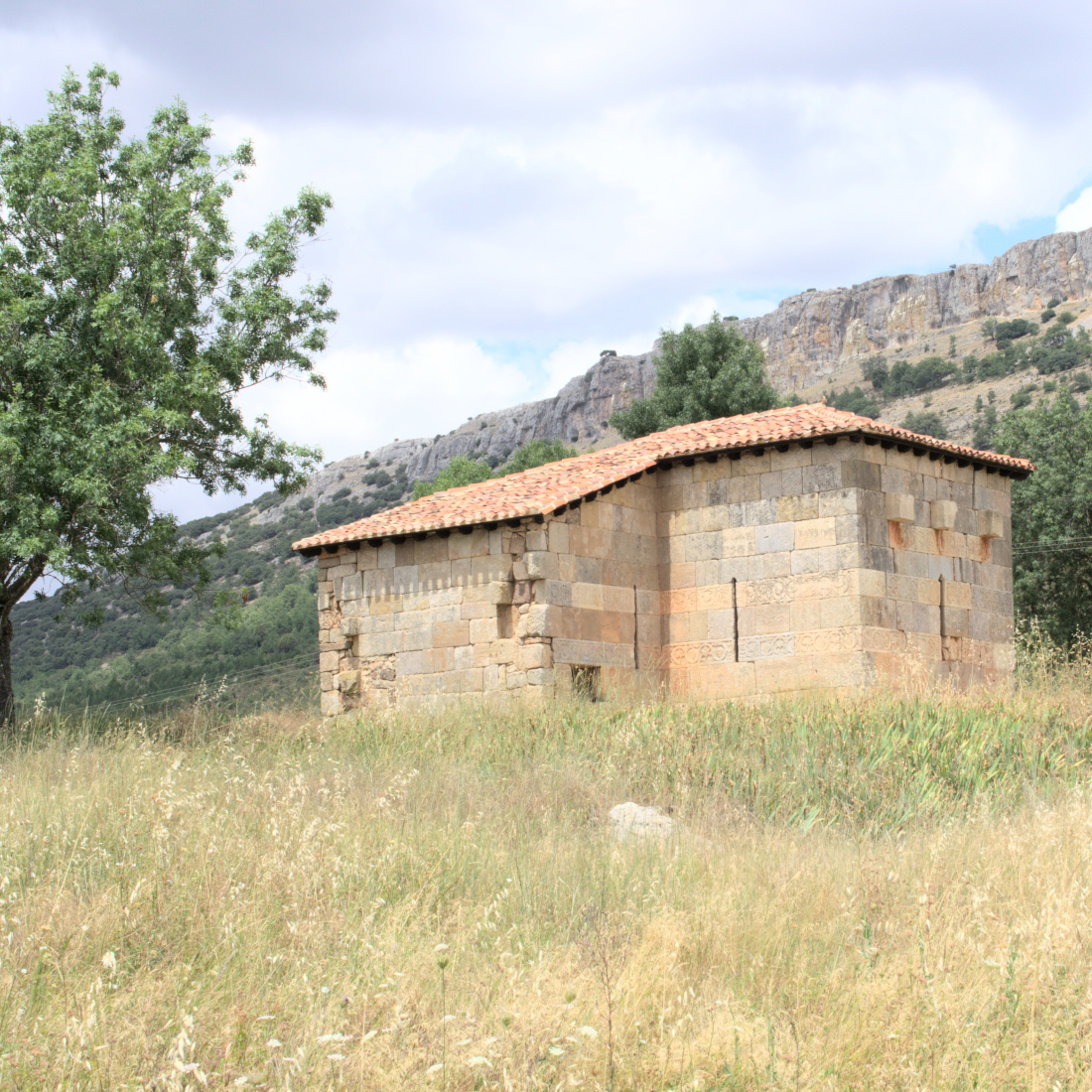 Часовня, освещённая солнцем, на фоне гор и хмурого неба.