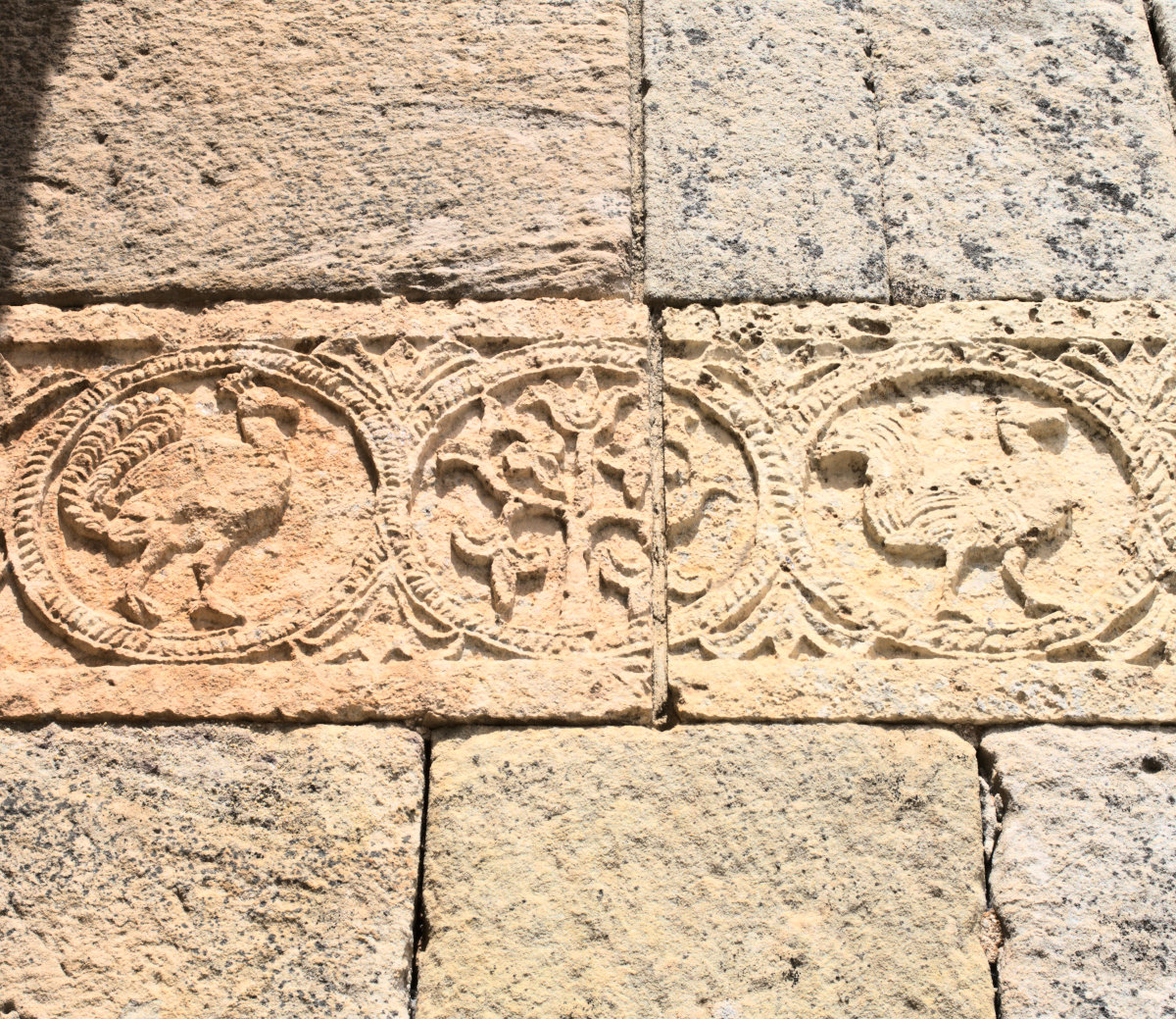 Изображение дерева или лозы посередине и фигуры птиц по бокам.