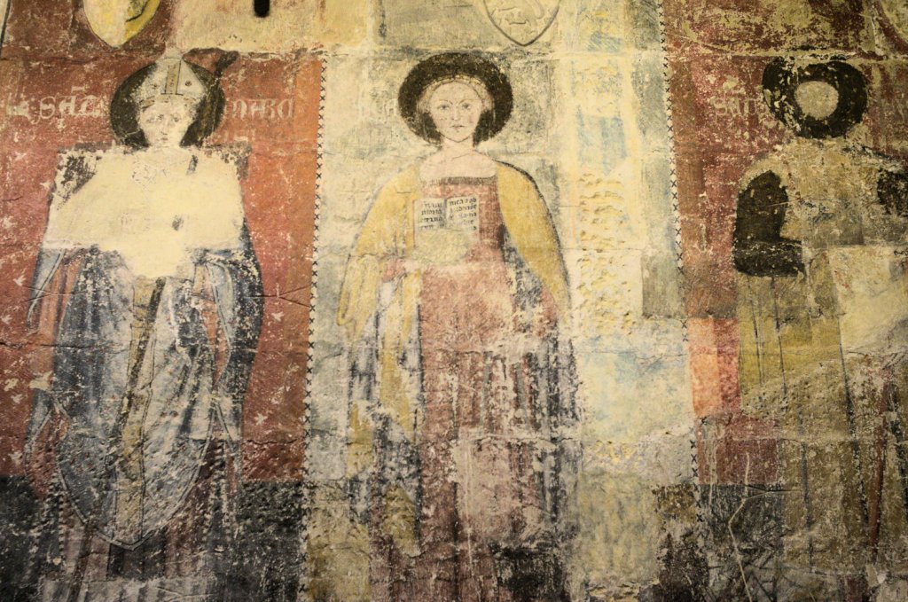 Три фигуры святых на поврежденной временем росписи.