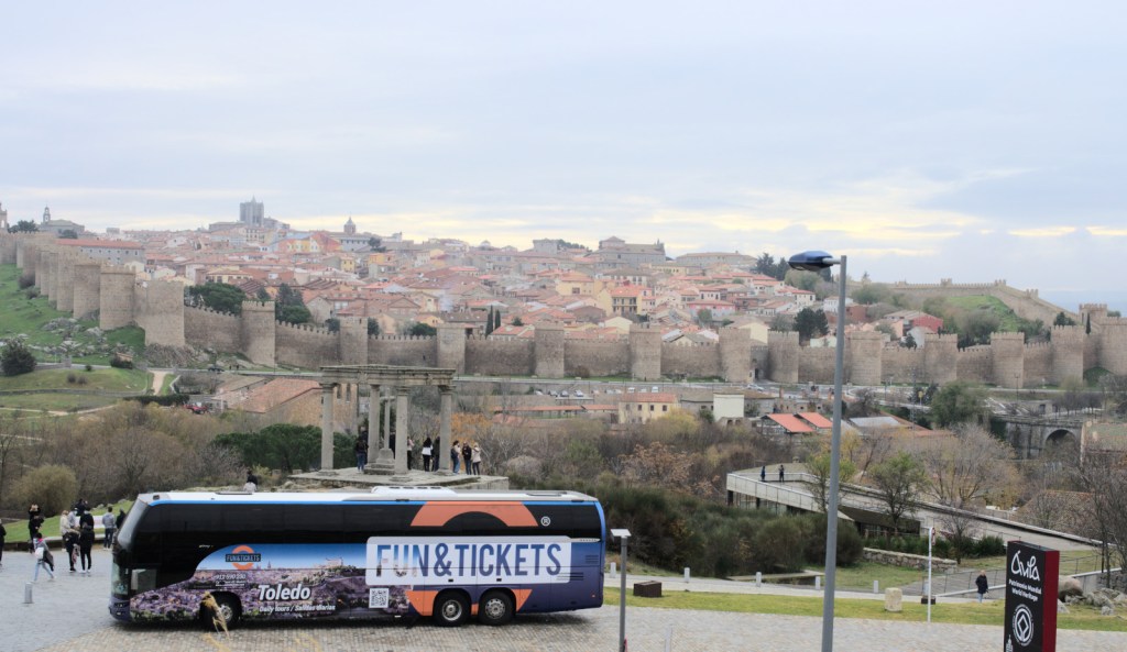 Вид, вмещающий укреплённую Авилу почти во всю её ширину; на ближнем плане — стоящий туристический автобус