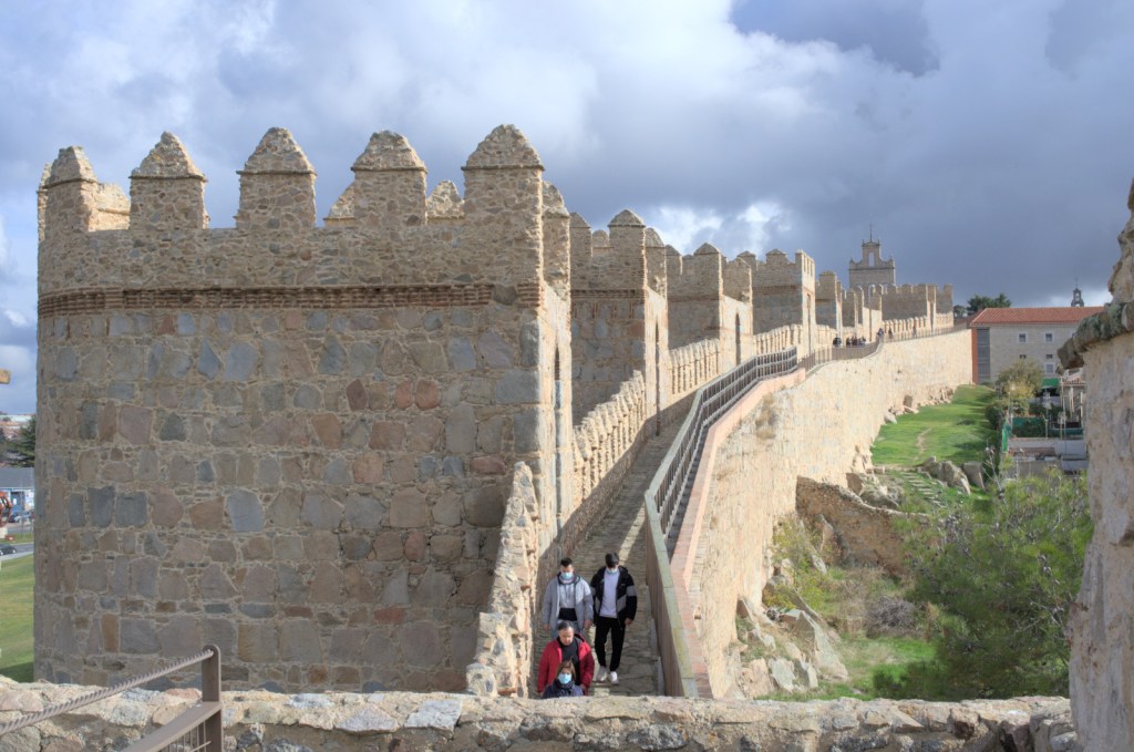 Вдаль уходит стена, башня за башней; на стене по дорожке прогуливаются люди
