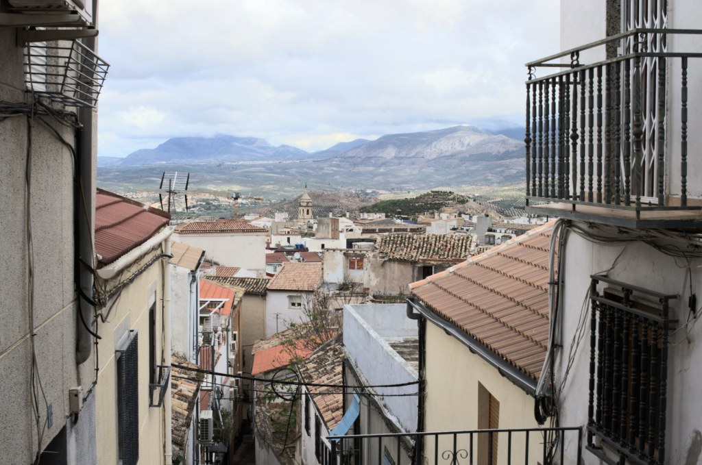 Вид вдоль улицы, уходящей вниз по склону. Вдали — горы.