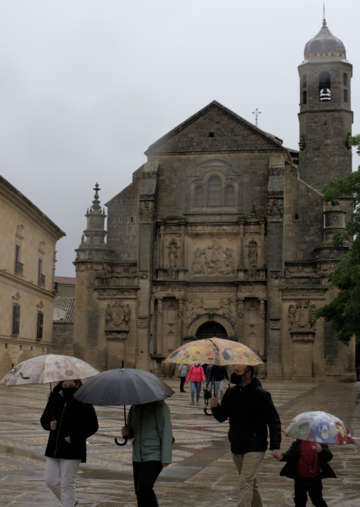 Люди с зонтиками шагают по площади, на заднем плане — церковь