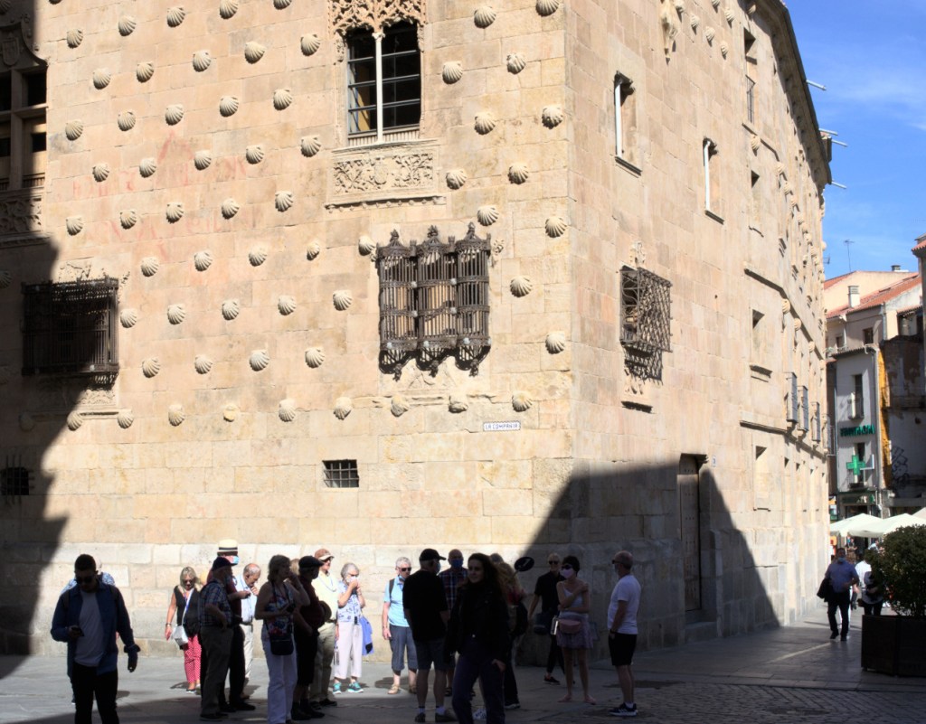 Люди на фоне освещённого фасада с каменными ракушками.