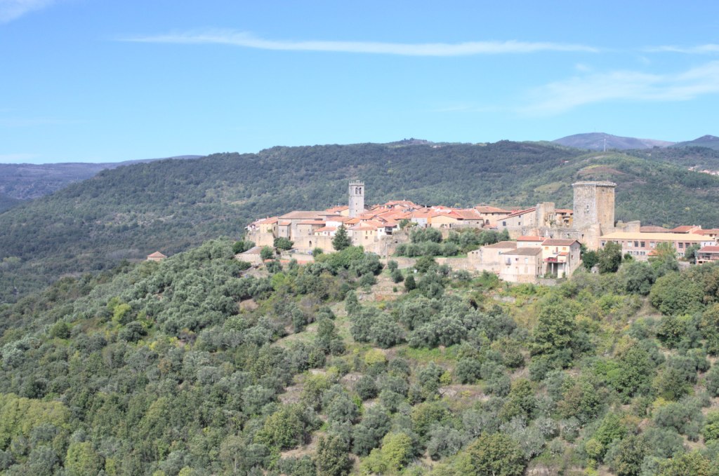 Две башни выделяются из группы домов, расположенной на вершине горы. Всё утопает в зелени.