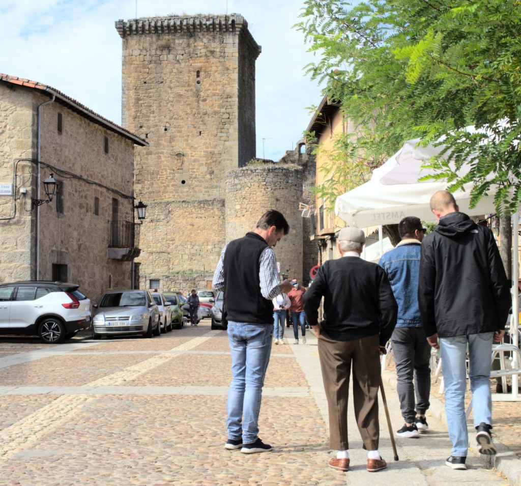 Люди идут по улице. Впереди — башня крепости.