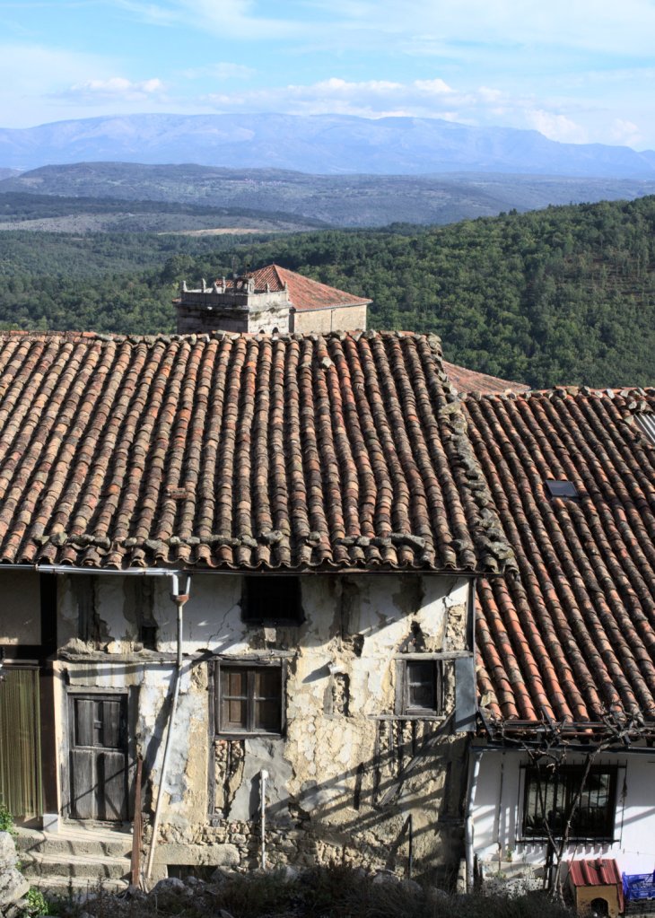 Облупленные фасады, черепичные крыши. Вдали — горы.