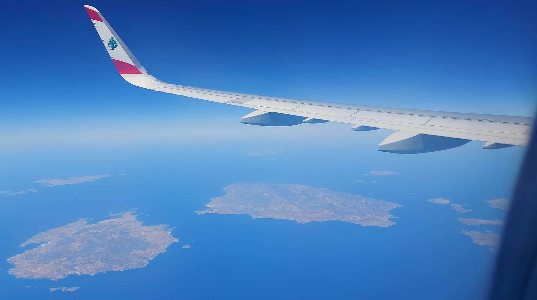 Вид в иллюминатор: крыло самолёта, внизу море и острова