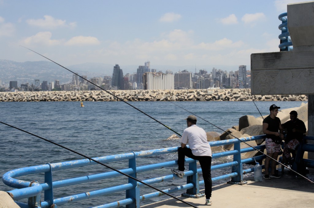 Рыбаки, море, вдалеке видно повреждённое зернохранилище, а за ним город