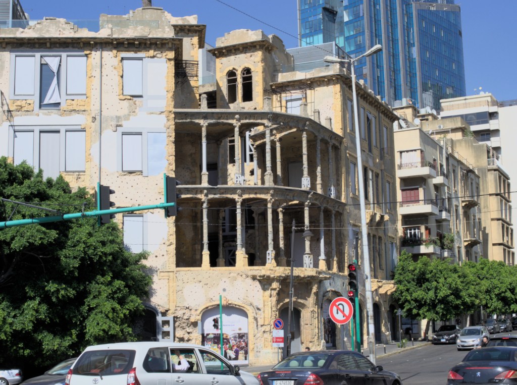 Здание с колоннадой на углу и со следами от обстрелов