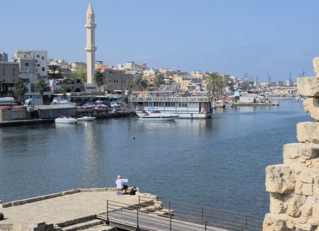 Вид на старый город с минаретом мечети. Видны причалы, вдалеке портовые краны. Под стенами крепости работает художник.