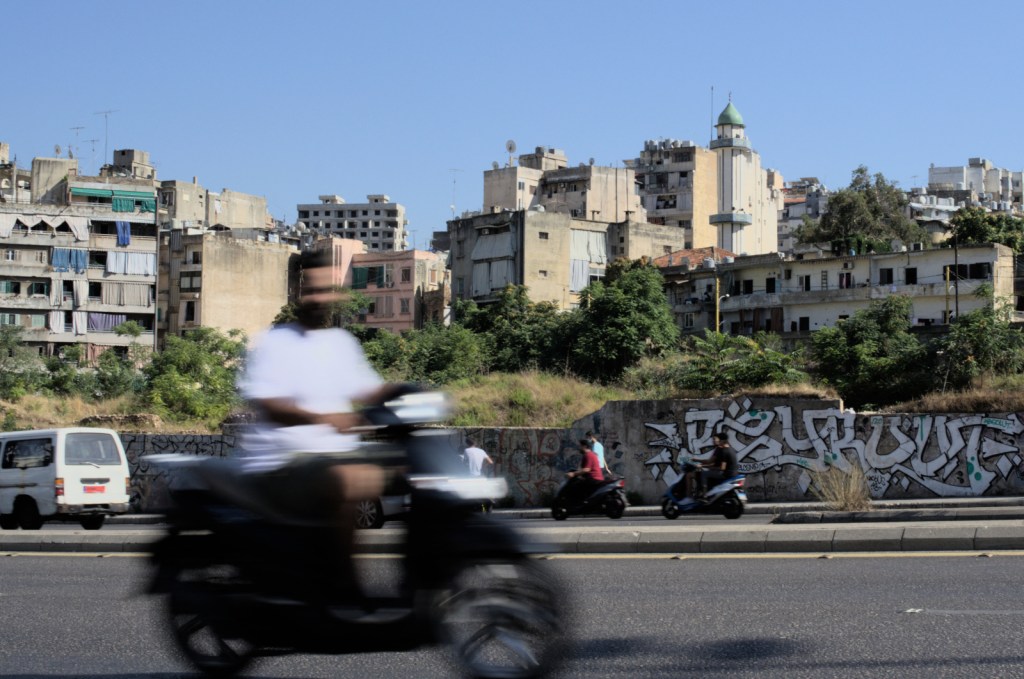 Мотоциклист проезжает по дороге на фоне граффити, жилых домов и мечети