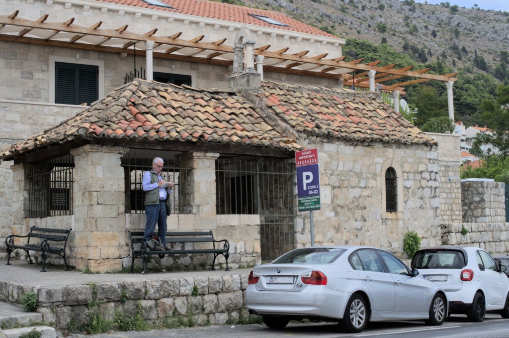 Часовня, на скамейке перед ней стоит мужчина и рисует в альбоме