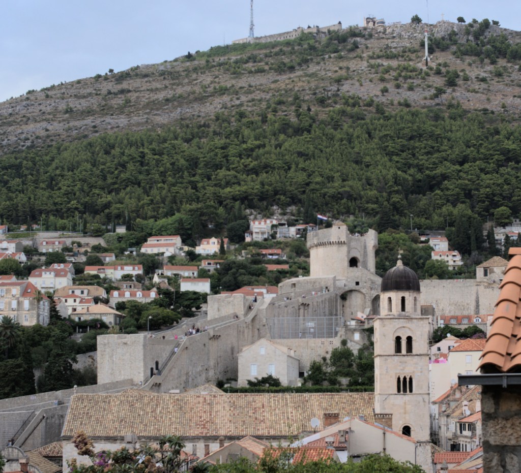 Церковь с колокольней, стена с башнями, склоны горы за ними