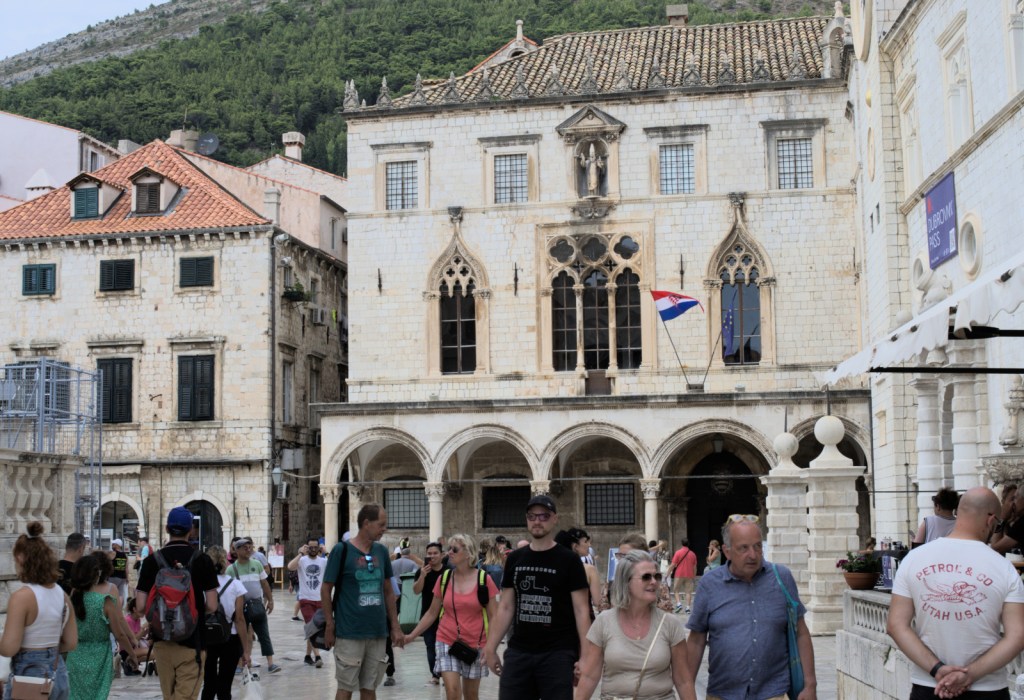 Люди идут по площади перед готическим дворцом