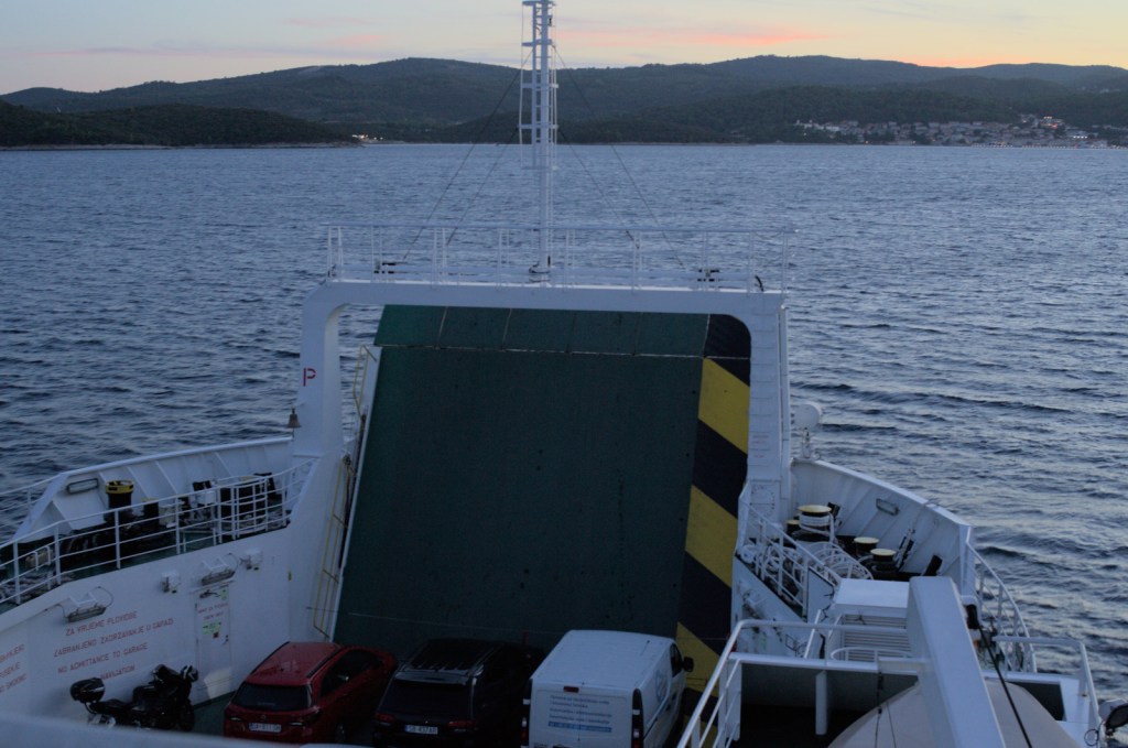 Паром с автомобилями движется в сумерки с сторону острова