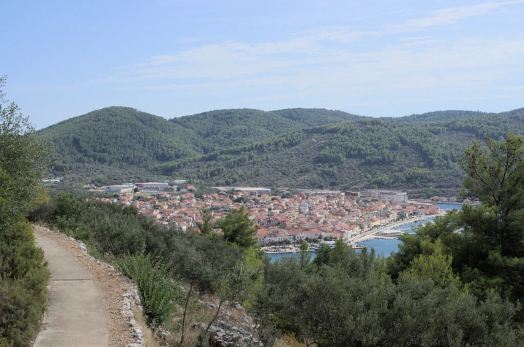 Далеко внизу портовый городок с красными крышами, за ним холмы