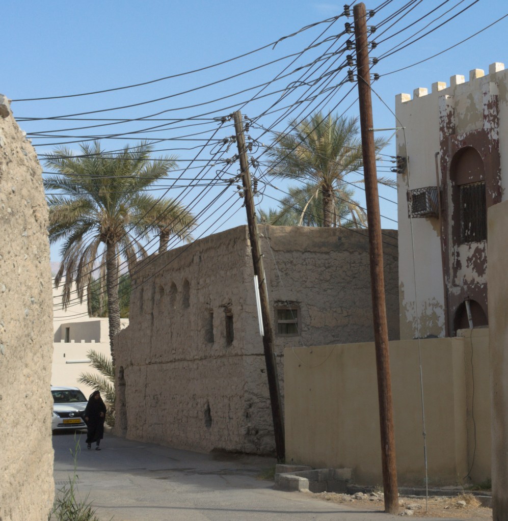 Улица, глинобитный дом, пальмы. Вдали идёт женщина в чёрном.