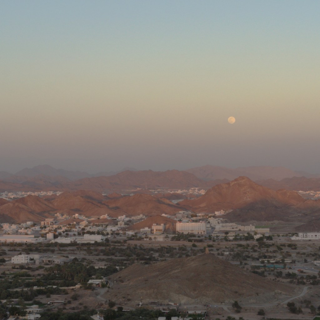 Вид на гористую местность, белые дома. В небе луна.