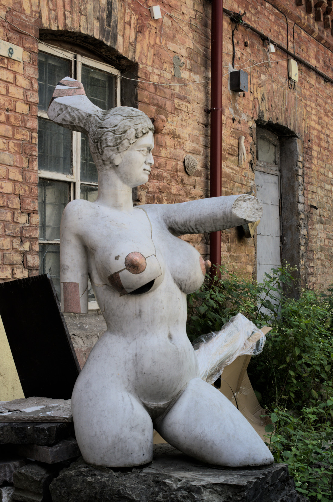 Скульптура обнажённой женщины на фоне кирпичной стены