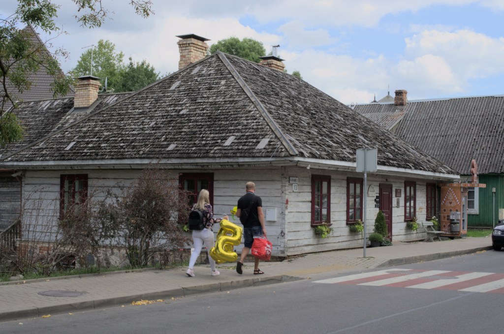 Люди идут по тротуару у деревянного дома