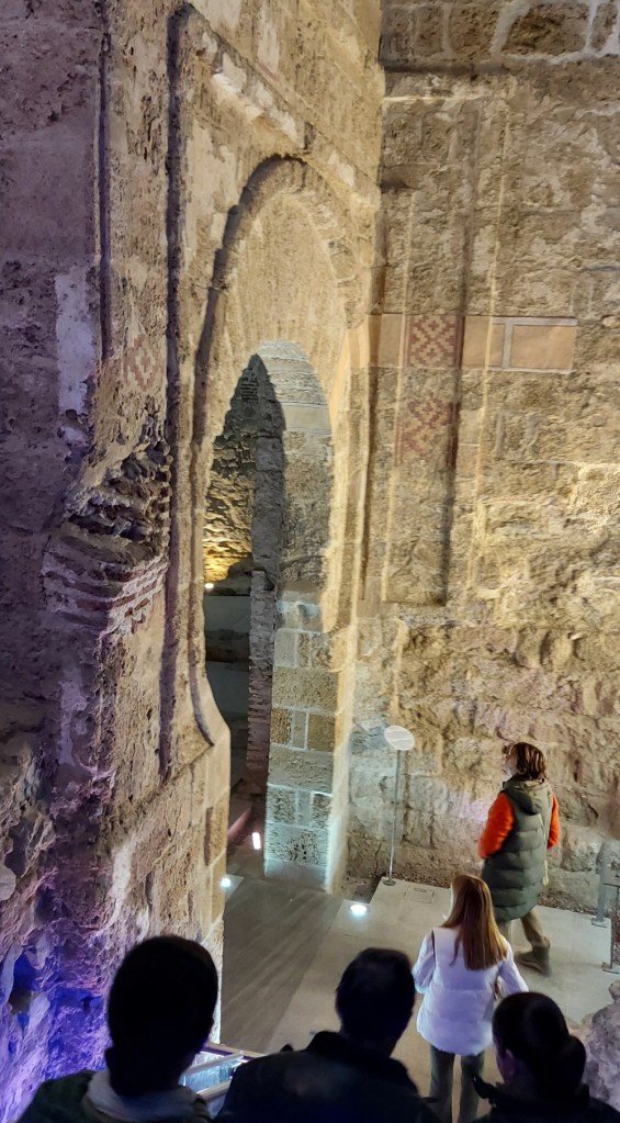 Группа посетителей спускается к арке старинных ворот в подземном музее