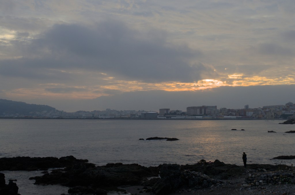 Лучи утреннего солнца пробиваются сквозь плотные тучи над прибрежным городом